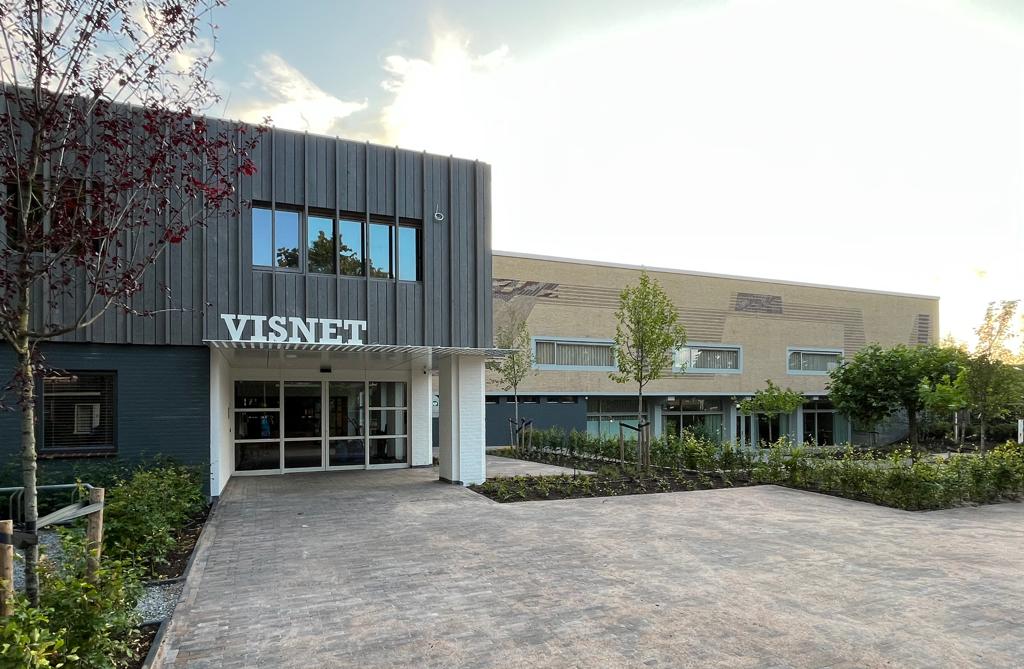 De entree van gebouw het Visnet in Huizen, waar het uitvaartcentrum van Rebel Uitvaart is gevestigd, met bestraat voorplein en jonge aanplant